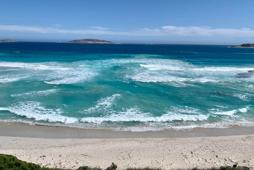 A blue and green swirling ocean with the beach in foreground.