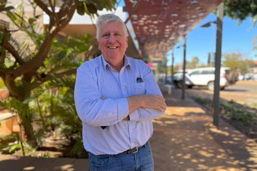 A middle aged man stands smiling with his arms crossed.