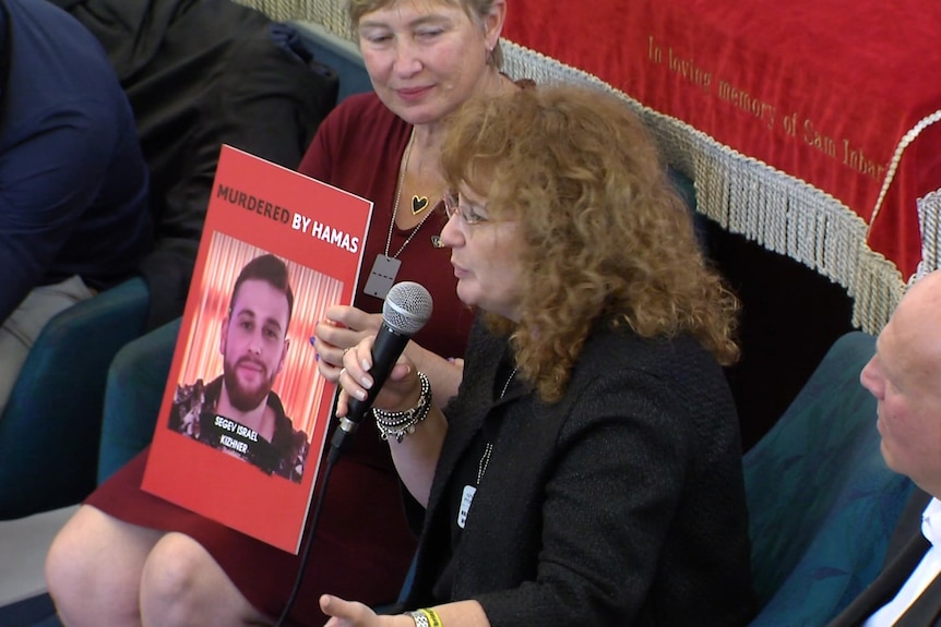 Tali Kizhner, a woman with brown curly hair and glasses holding a microphone. A photo of her son next to her