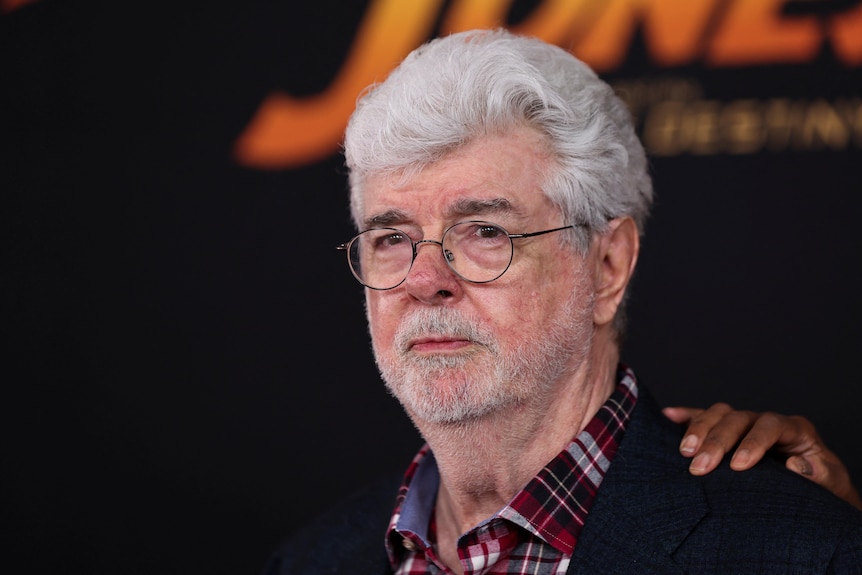 A close up of George Lucas wearing glasses anda suit at a film premier.