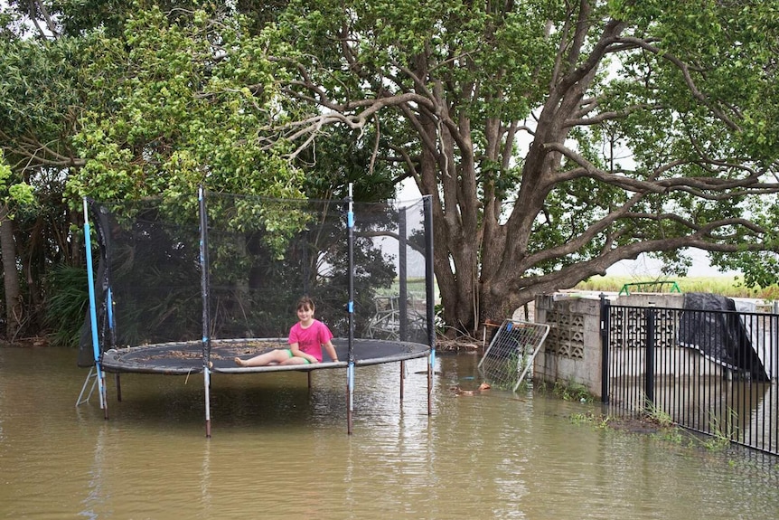 A young girl sits on her trampoline in her flooded backyard, north of Bundaberg on October 19, 2017