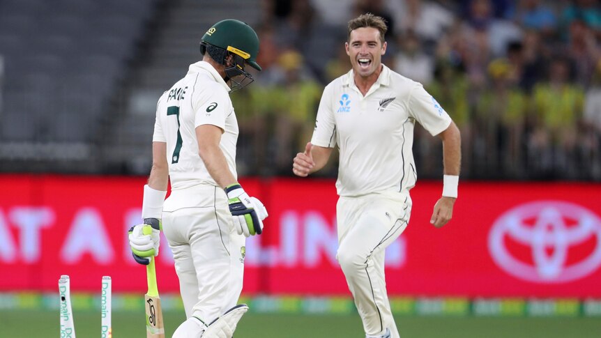 Tim Southee smiles and looks at Tim Paine, who has his head down, as he runs past him with the stumps knocked down.