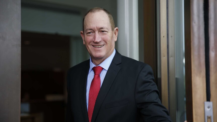 Fraser Anning smiles while holding open the door at Parliament House on his first day.