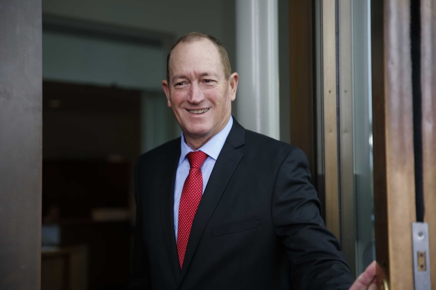 Fraser Anning smiles while holding open the door at Parliament House on his first day.
