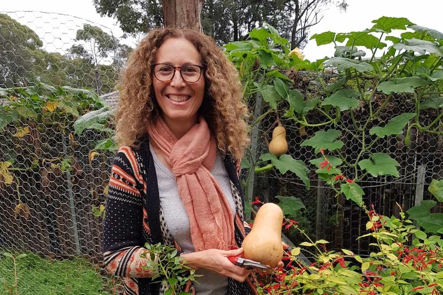 Karen Wakil holding a pumpkin sitting in a garden with plants around her 