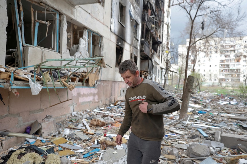A man walks on debris past the wreckage of a residential building that was heavily damanged by shelling.