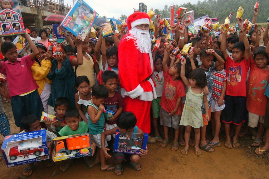 Children stand holding toys alongside a man dressed as Santa Claus