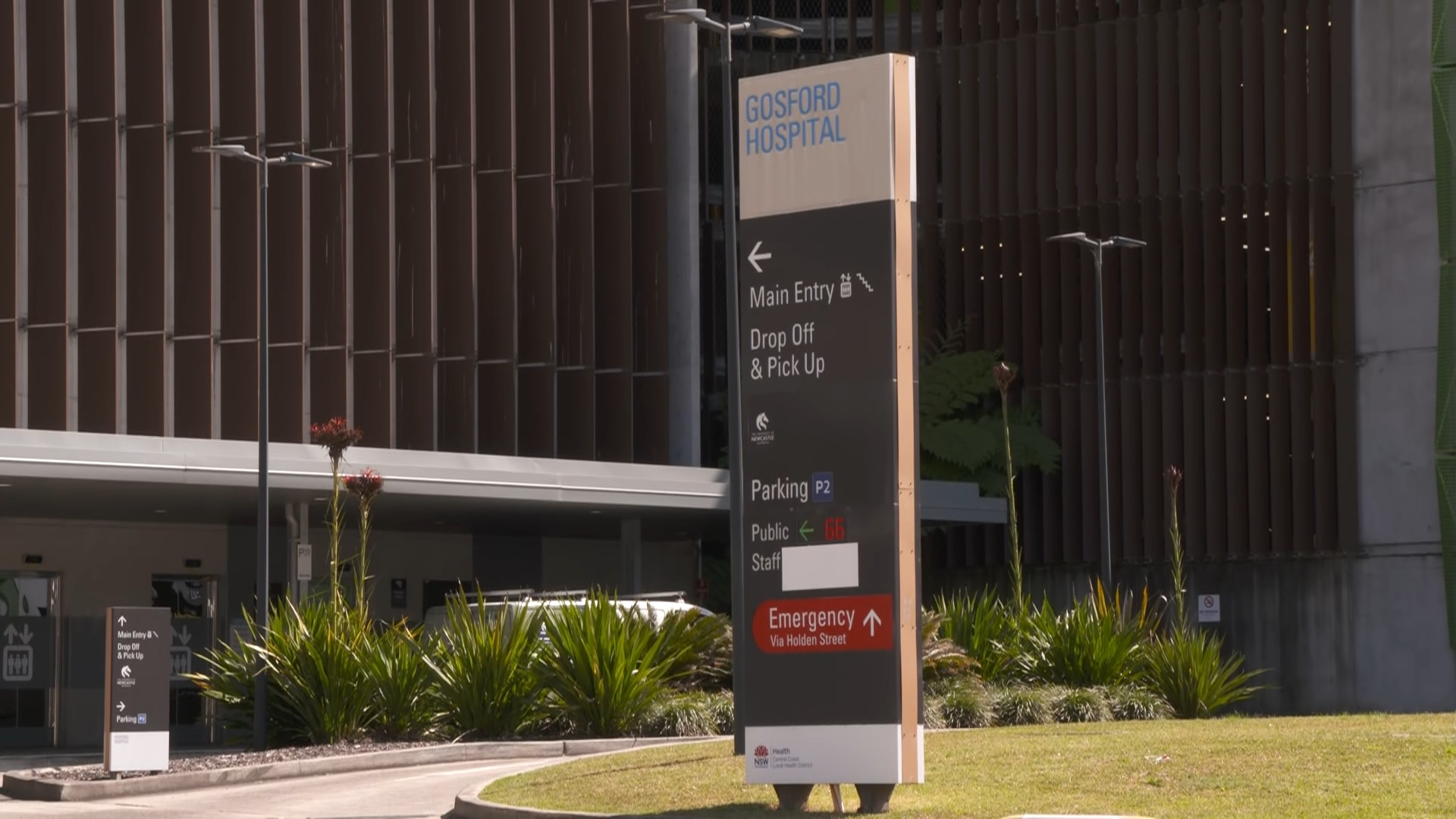 A long narrow sign that reads "Gosford Hospital" outside a large building.