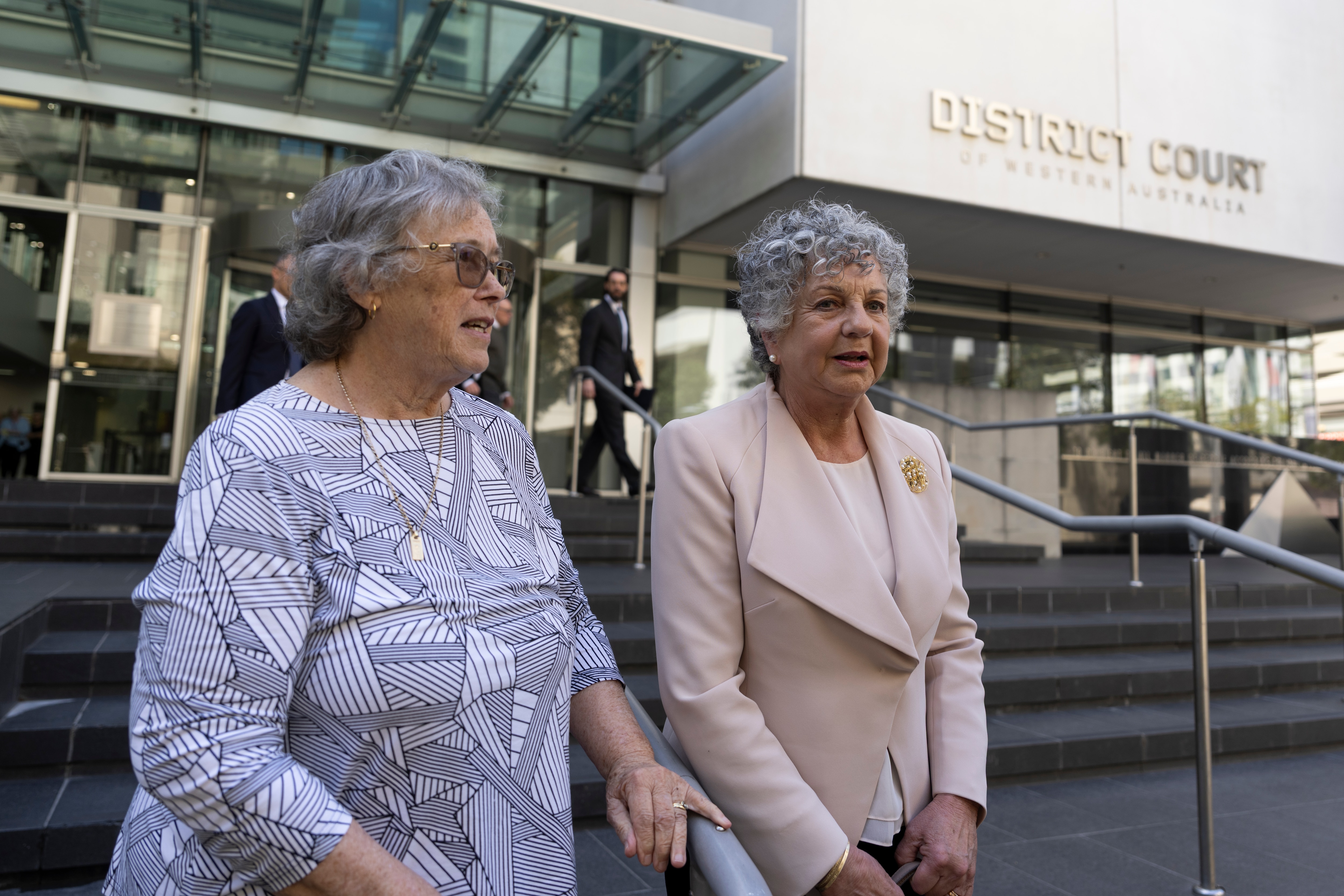 Two women with short grey hair stands in front of a court building. 