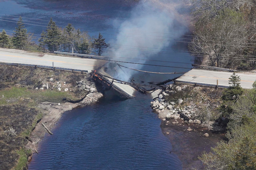 A collapsed bridge over a river on fire with smoke billowing out of it