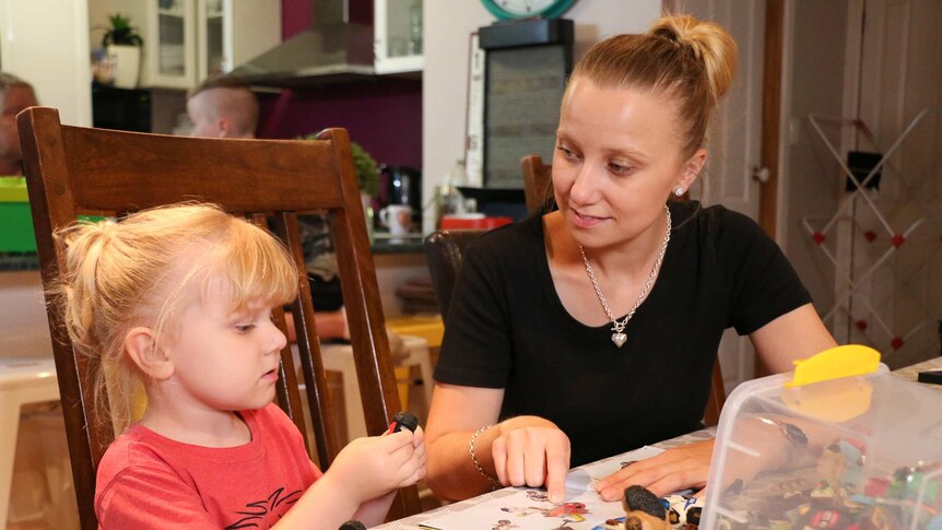 Cara and her son Ryland sit at a kitchen table playing with toys.