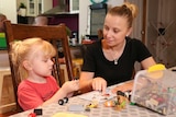 Cara and her son Ryland sit at a kitchen table playing with toys.
