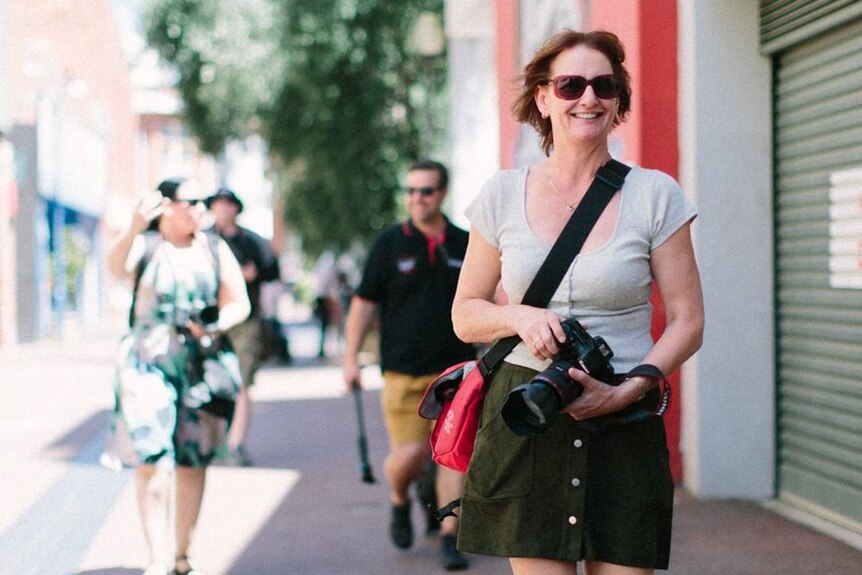 Liz Barker walking down a city street holding a digital camera.