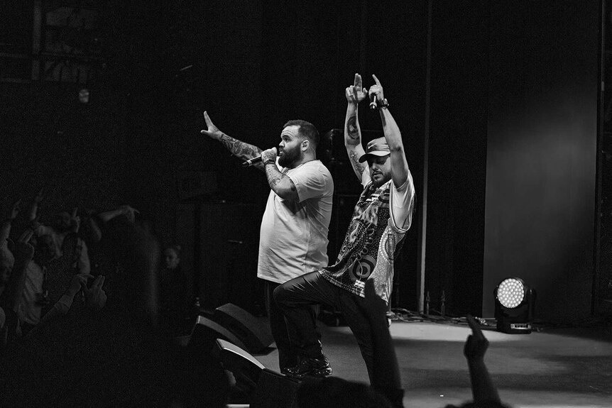 Black and white photo of rappers Briggs and Nooky on stage with arms raised at Sydney Opera House.