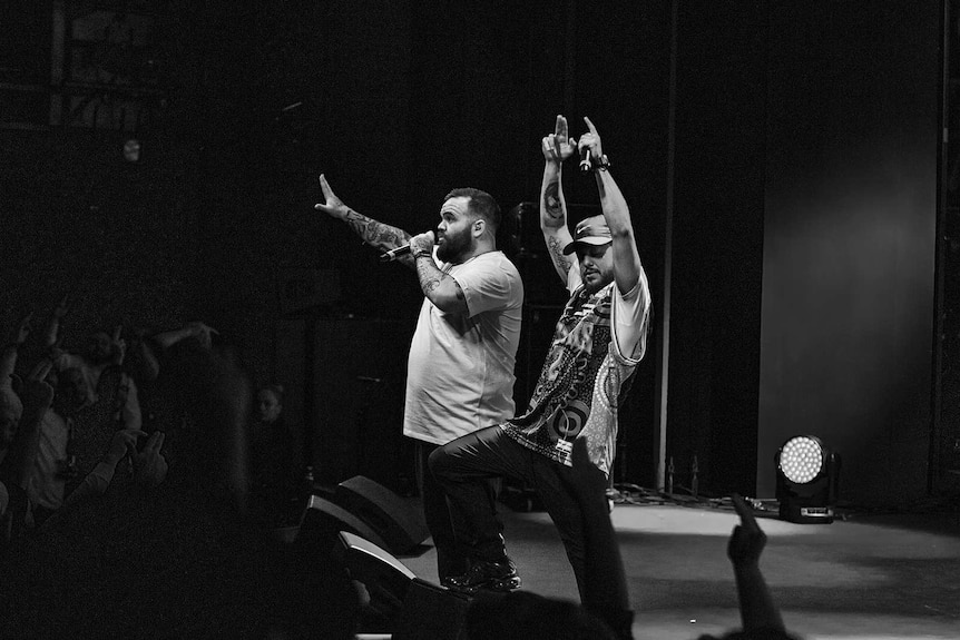 Black and white photo of rappers Briggs and Nooky on stage with arms raised at Sydney Opera House.