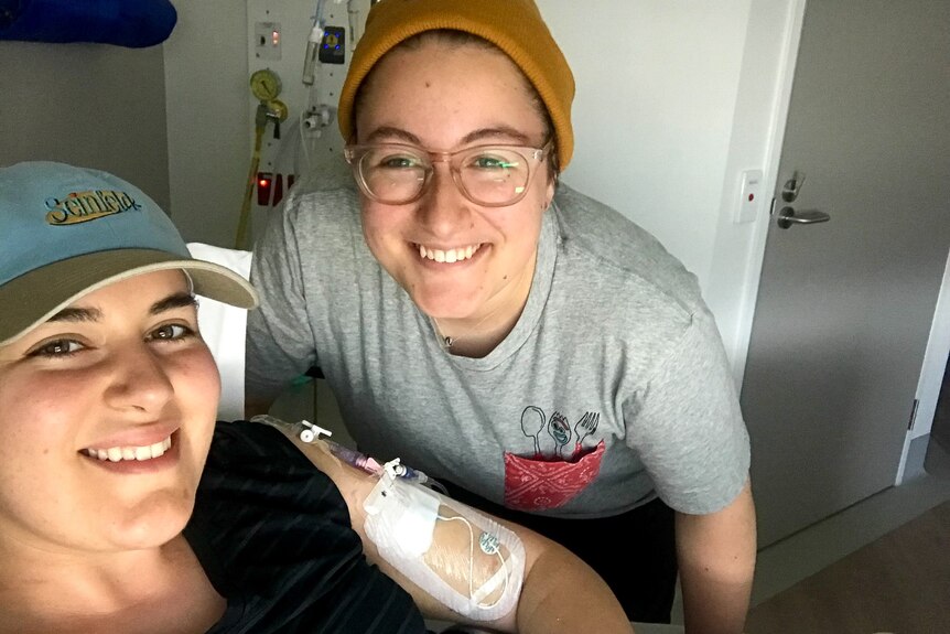 Two women in hospital smiling at the camera, one with tubes coming out of her arm
