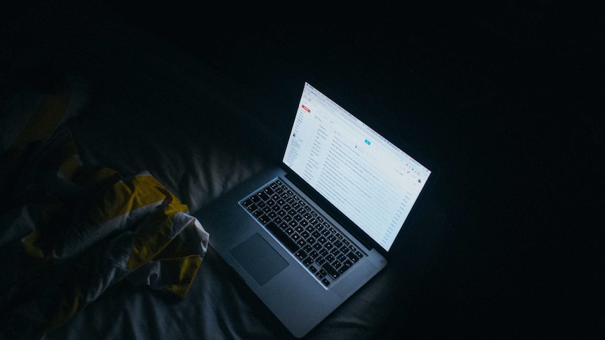 A Mac laptop resting on a bed in the dark