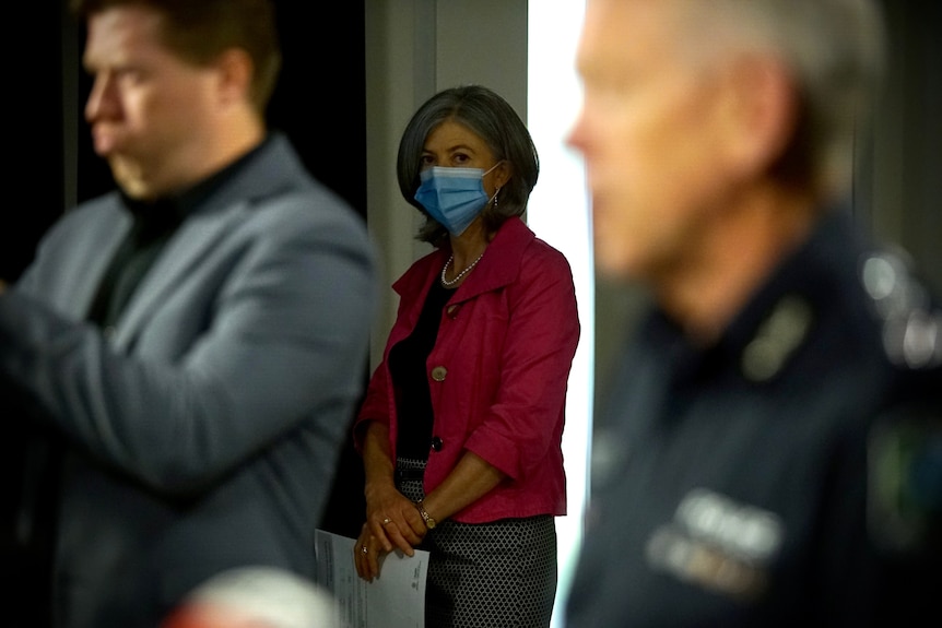 A woman wearing a pink jacket and a face mask standing between two men