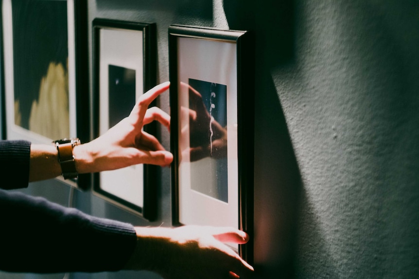 A hand reaches out to straighten a picture on the wall.