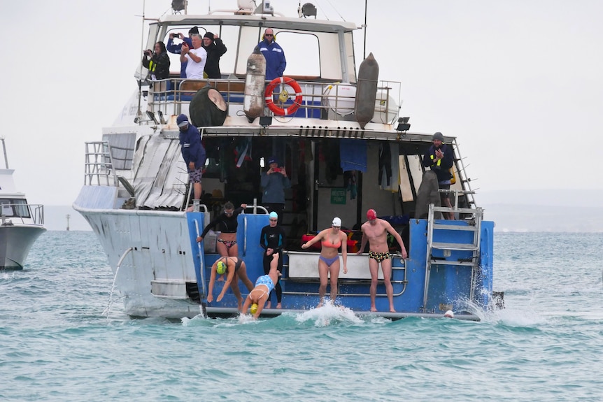 People in bathers jump off a boat into the ocean. 