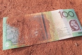 A $100 bill in red dirt
