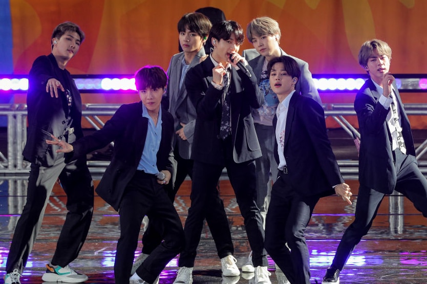 BTS members sing into their microphones on stage while wearing suits