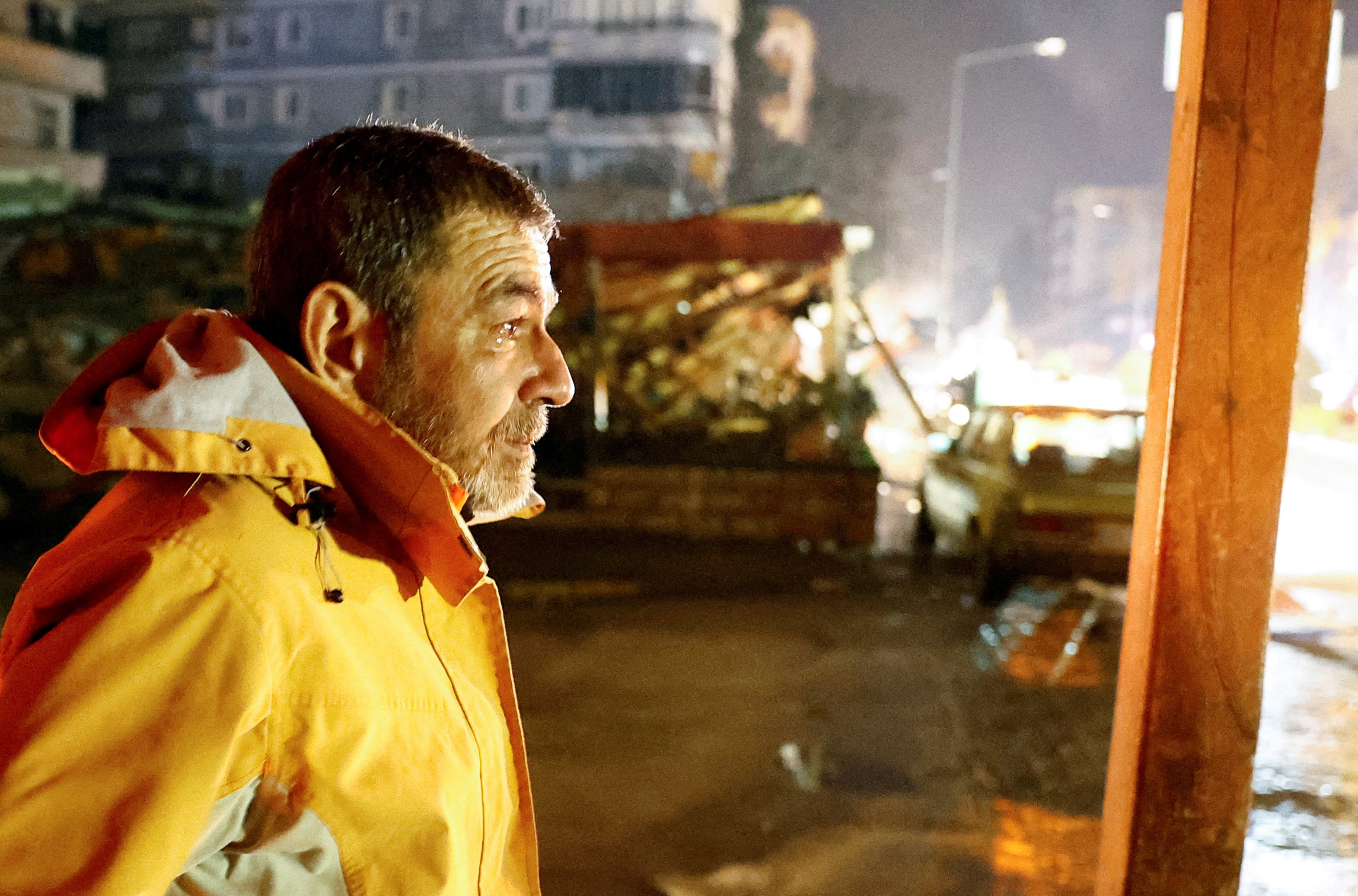 A man in a street looks on with tears in his eyes, in front of earthquake debris at night