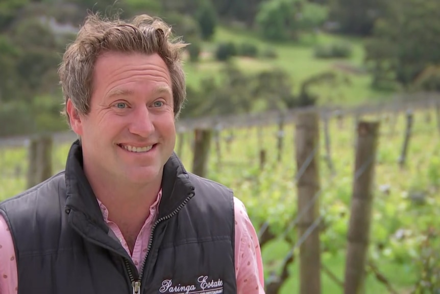 A man smiling with grapevines in the background.