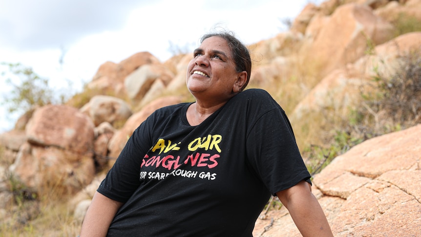 A woman wearing a black top sits on a rock and looks at the sky