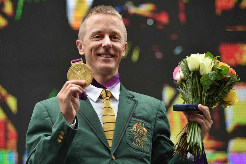 A race walker wearing an Australian blazer holds a gold medal in one hand and a bouquet in the other.