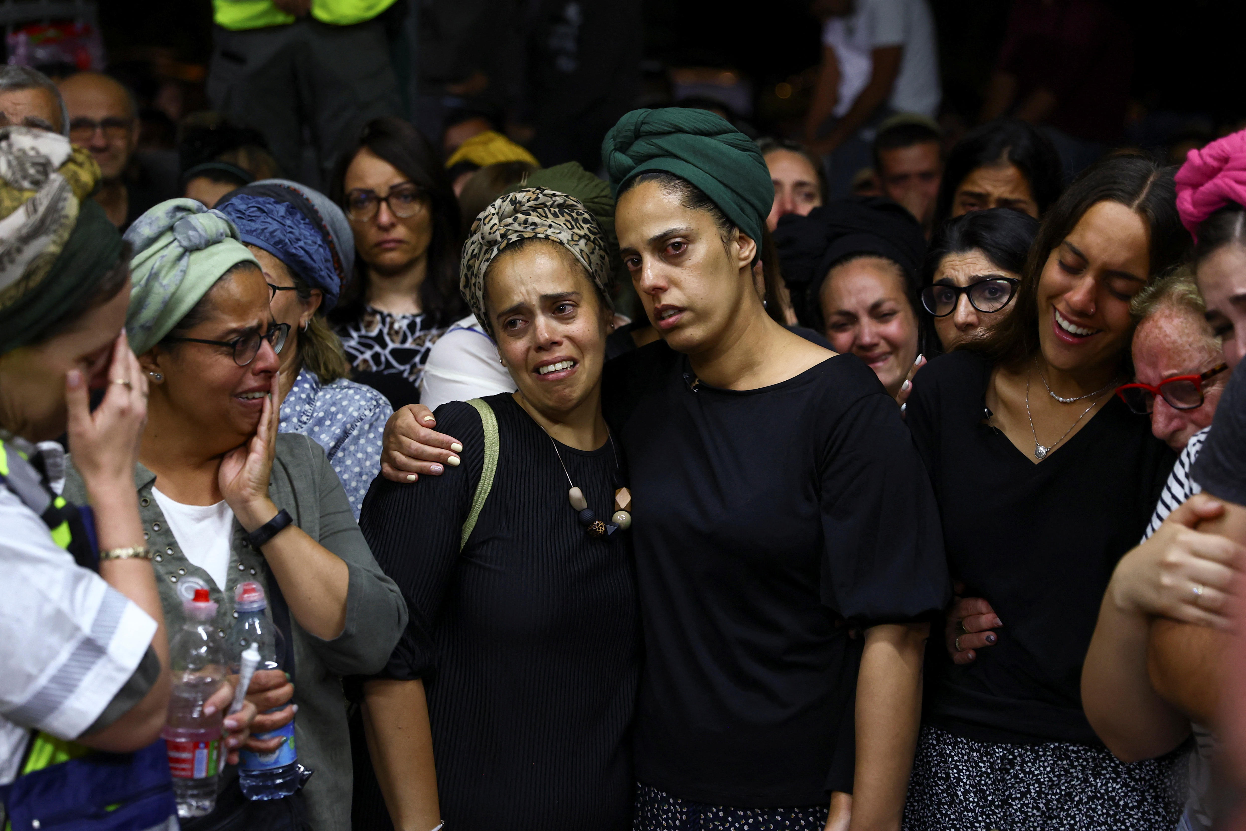 A group of mourners with their arms around each other crying.  