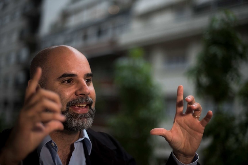 Maximiliano Ruiz, a bald man with a greying beard, raises his hands as he speaks during an interview.