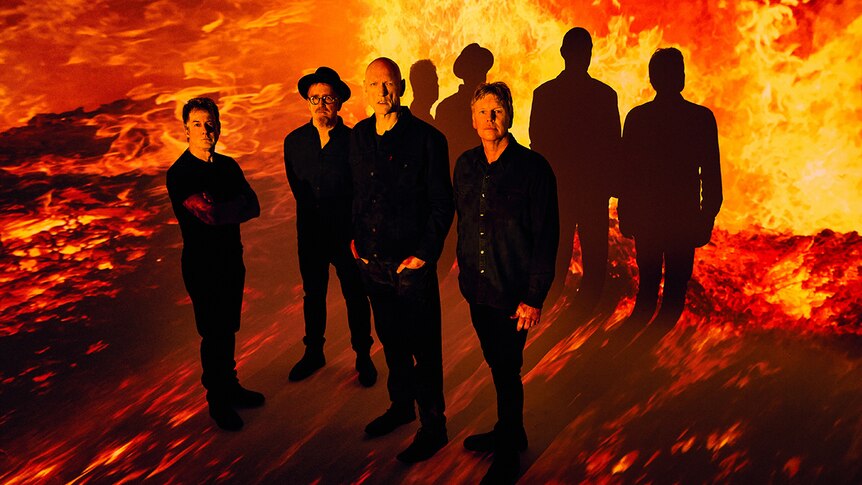 Four members of Midnight Oil stand in a fiery pit wearing black