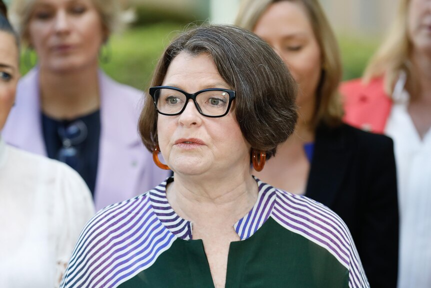 Ged Kearney with short brown hair and glasses at a press conference with a group of other female politicians behind her