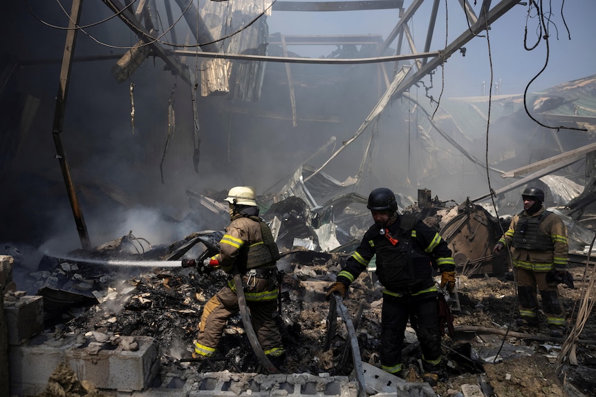 Two firefighters aim a hose at smouldering paper in the ruins of a burnt warehouse 