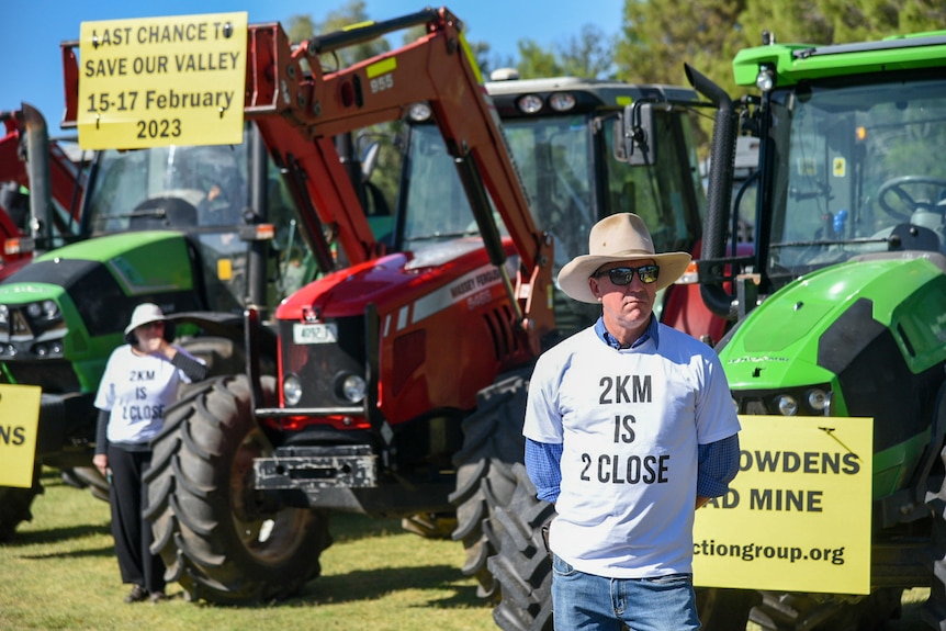 Homme debout devant des panneaux de protestation et des tracteurs