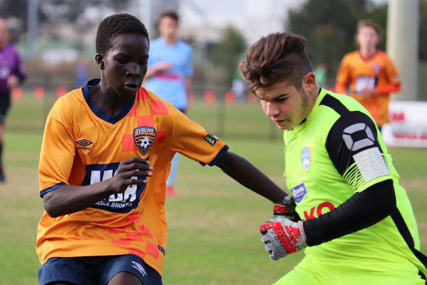 young boy in orange top competing for the ball against another boy