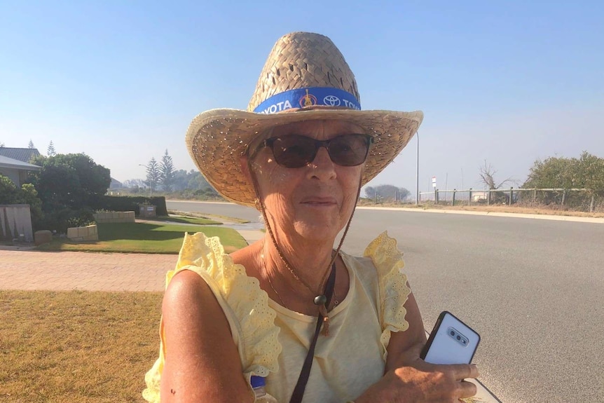 A woman in sunglasses and hat walks around her street with smoke in the background