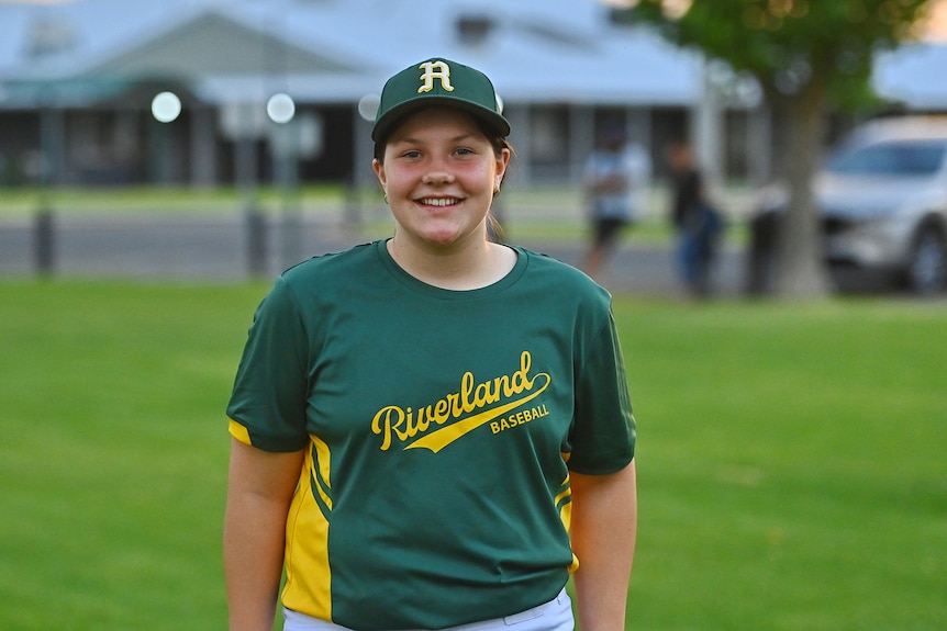 A smiling teenage girl in a baseball uniform.