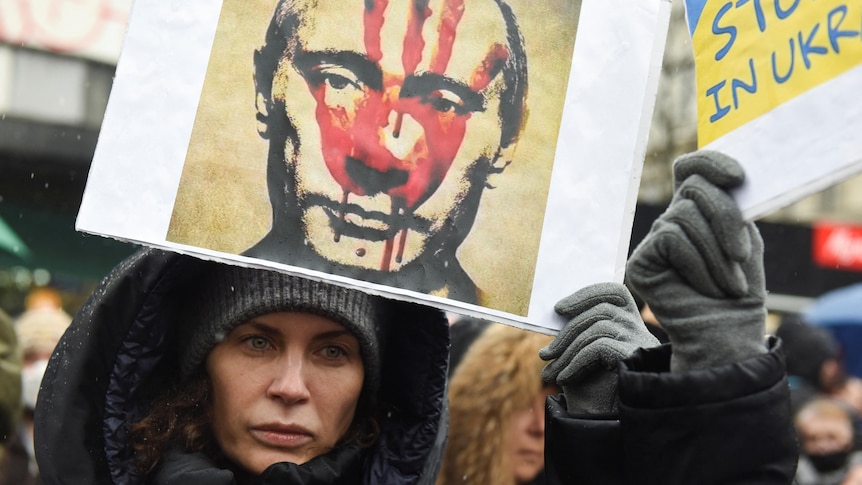 A woman holds a poster of Putin's face with a bloody hand across it. 