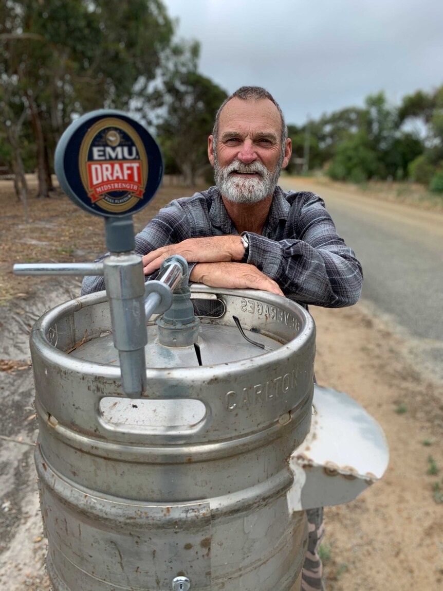 A man leans against a mailbox that has been made out of a modified stainless steel beer keg.