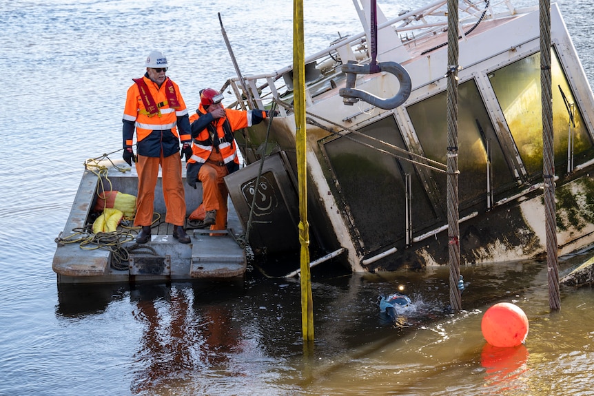 Two workers in high-vis clothing as a ship is pulled from the water.