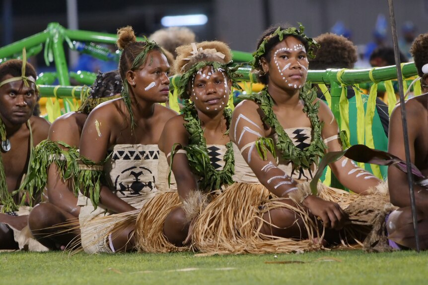 Performers wearing traditional dress sit on the ground at the Pacific Games opening ceremony.