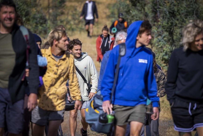 People carrying bags walk along a dirt track