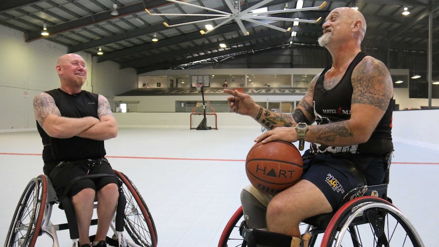 Two men in wheelchairs face each other on a basketball court.