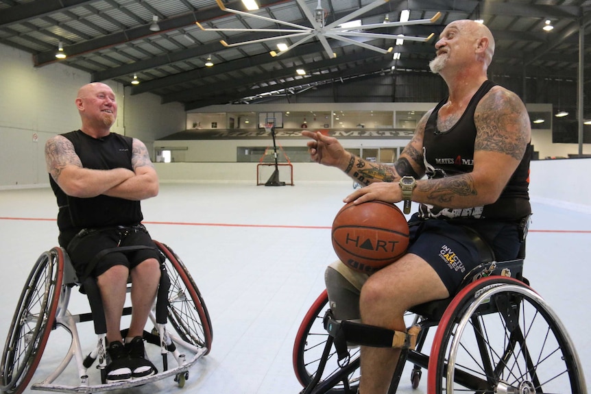 Two men in wheelchairs face each other on a basketball court.