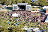 An aerial shot of a large crowd in front of a huge stage at an outdoor festival.