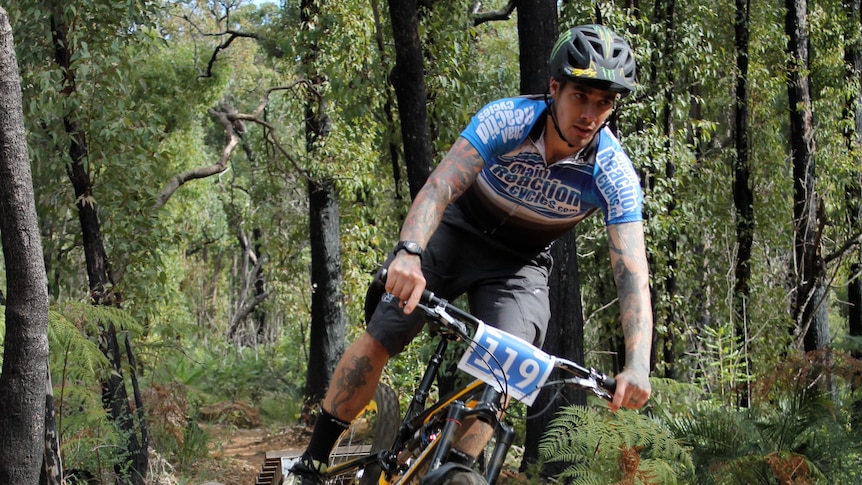 man wearing helmet on a mountain bike which is on a track in a forest of native Australian trees.