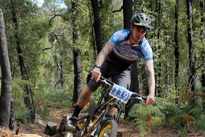phot of man wearing helmet on a mountain bike which is airborne above a track in a forest of native Australian trees.