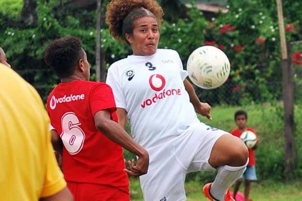 Lavenia juggling the ball with her knee during a game. She is wearing a white stripe with red trim.